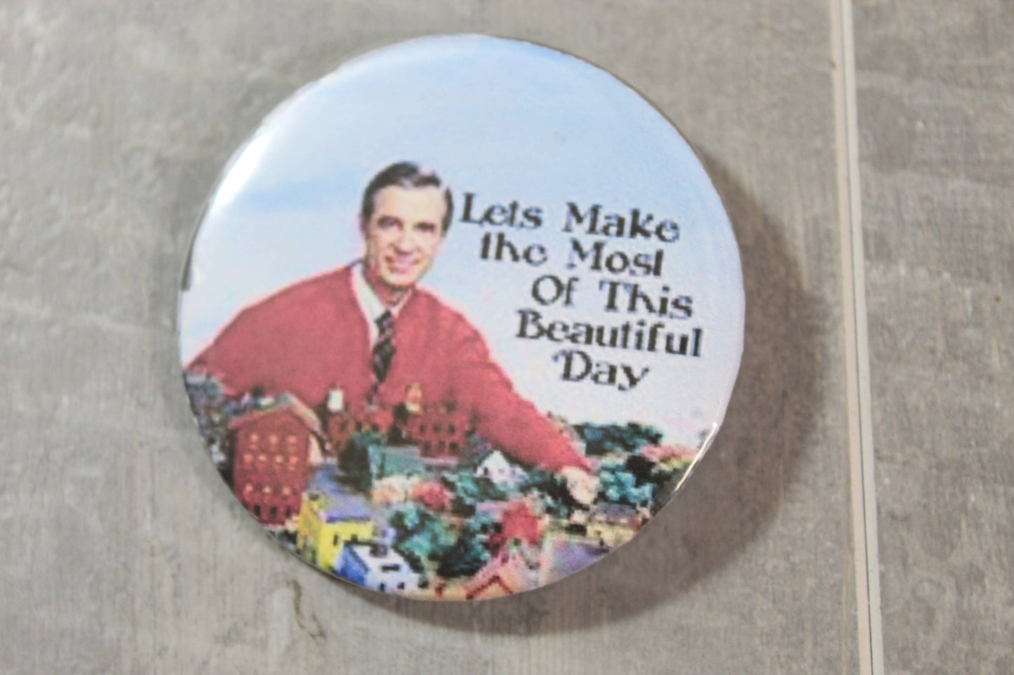 Mr Rogers on a button that says let's make the most of this beautiful day